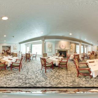 A spacious dining room with elegantly set tables and chairs, featuring a fireplace and carpeted floors.