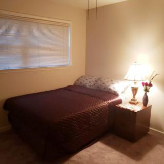 A cozy bedroom with a neatly made bed, lit by a lamp on the nightstand.