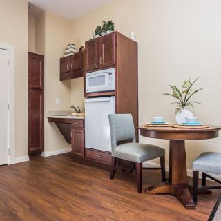 A cozy kitchenette with a small dining area, featuring wood cabinets, a microwave, and two chairs around a round table.