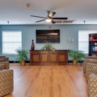A cozy living room featuring sofa chairs arranged around a television, with a wooden floor and decorative elements such as plants and a vase.
