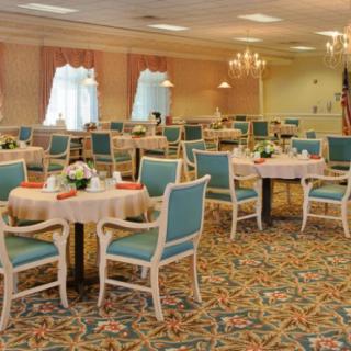 An elegantly furnished dining room with neatly arranged tables and chairs, decorated with floral arrangements and illuminated by chandeliers.