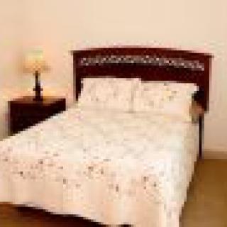 A cozy bedroom featuring a neatly made bed with floral bedding, accompanied by a nightstand and lamp.