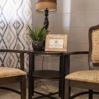 A cozy corner with two chairs flanking a small table, adorned with a lamp, plant, and framed picture.