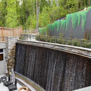 A serene outdoor patio featuring a cascading waterfall with lush greenery and a painted mural wall.