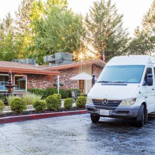 A white van parked in front of a modern building surrounded by trees and greenery, illuminated by the morning sun.