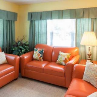 A cozy living room with vibrant orange couches and green curtains.