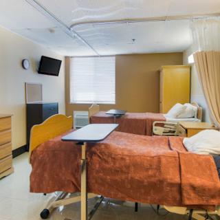 A view of a hospital patient room featuring two beds, bedside tables, and a television.
