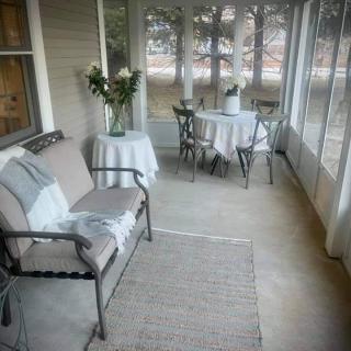 A cozy porch featuring a bench, a table with chairs, and a vase with flowers.