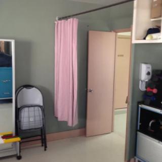 A room with a folding chair, pink curtain, and open door, possibly in a clinic or hospital setting.