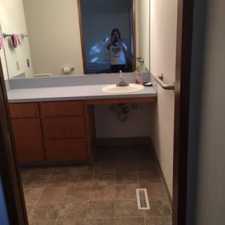 A bathroom with a large mirror and sink, featuring wooden cabinets and a tile floor.