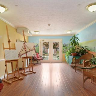 A bright and inviting art studio with easels, plants, and a wooden floor.