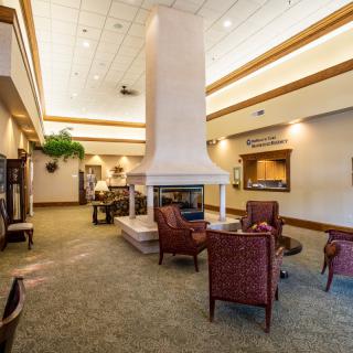 A spacious lobby with a central fireplace, surrounded by comfortable chairs in a well-lit area.