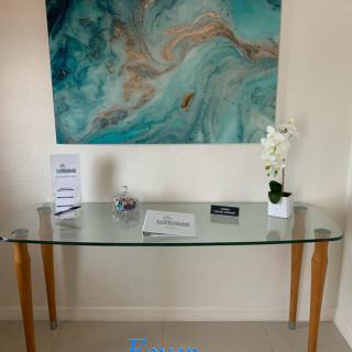 A glass table in an interior setting with a decorative orchid plant and abstract artwork on the wall.