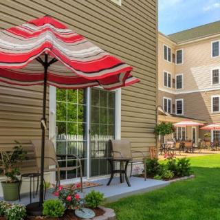 A cozy outdoor patio area with a red and white striped umbrella, surrounded by a lush green lawn next to a building.