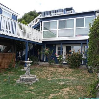 A two-story house with a balcony, featuring a small garden and fountain in the yard.