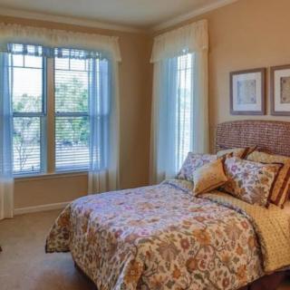 A cozy bedroom with a bed, patterned bedding, and large windows with sheer curtains.