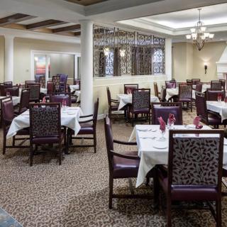 An elegant restaurant dining room with neatly arranged tables and chairs, featuring chandeliers and a patterned carpet.