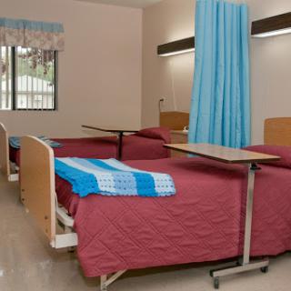 A clean and organized patient room in a healthcare facility, featuring two beds and decorative curtains.