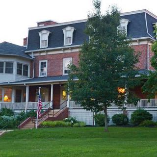 A large brick house with a porch and surrounding garden, photographed in the evening.