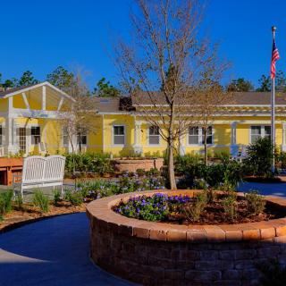 A bright yellow building with a landscaped garden and flag under a clear blue sky.