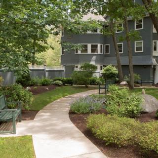 A peaceful garden with a winding pathway and benches, surrounded by trees and well-maintained landscaping in front of a residential building.