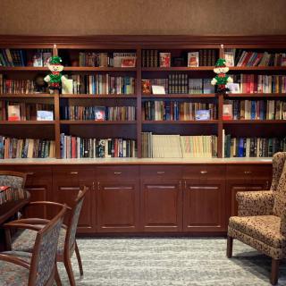 A cozy library room with a large wooden bookshelf filled with books, adorned by green lamps and accompanied by comfortable chairs.
