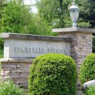 Entrance sign to Courtyard Estates surrounded by greenery and stonework.
