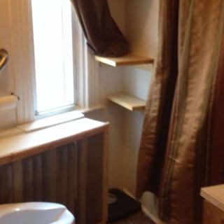 A cozy bathroom with a window, sink, and shelves adorned with curtains.