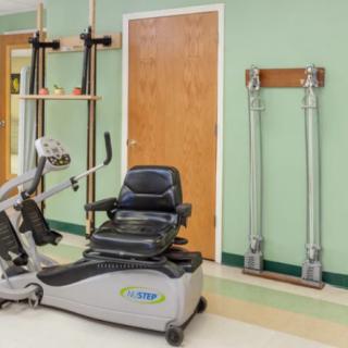 A therapy room with an exercise bike and rehabilitation equipment against a green wall.