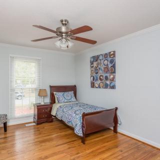 A simple bedroom with a single bed, wooden flooring, and a ceiling fan.