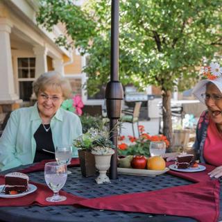 Two elderly women enjoying a meal together on a sunlit patio.