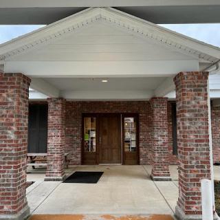 The entrance of a brick building featuring elegant columns and a spacious porch.