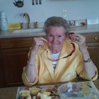 An elderly woman smiles while peeling apples in the kitchen.
