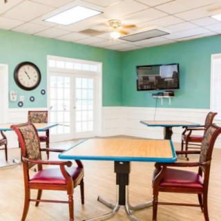 A bright dining area with several tables and chairs, featuring a wall-mounted television and a clock.