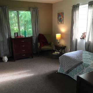 A cozy bedroom with a bed, dresser, and chair near the window.