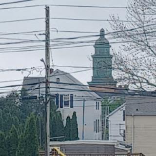 A view of a building with a prominent tower, surrounded by power lines and residential structures.