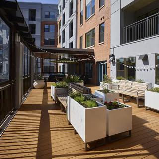 A modern apartment building features a spacious outdoor patio with seating and planters.