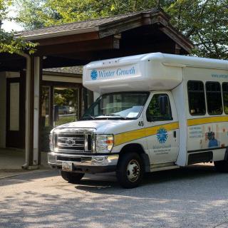 A shuttle bus parked at a stop in a wooded area.