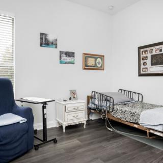 A cozy nursing home room featuring a hospital bed and a comfortable armchair, decorated with framed wall art.