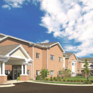 A modern residential building with a landscaped entrance under a bright blue sky.