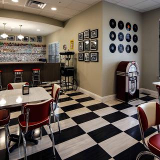 A retro-style diner with black and white checkered flooring, red chairs, a jukebox, and vintage decor.