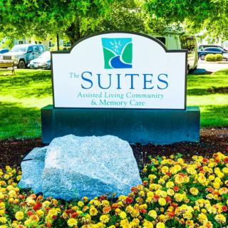 A landscaped sign for 'The Suites' healthcare center surrounded by flowers.
