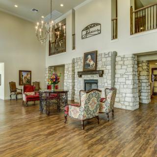 Spacious living area with high ceilings, elegant chandelier, and a cozy fireplace surrounded by comfortable seating.