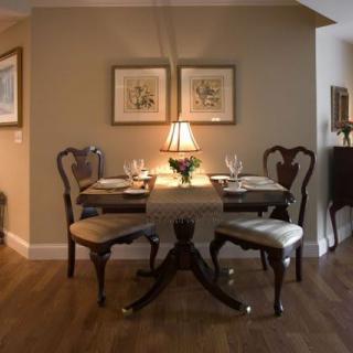 A cozy dining room with a wooden table set for four, adorned with a central lamp and artwork on the walls.