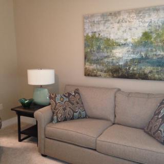 A cozy living room with a beige sofa, decorative pillows, a side table with a lamp, and abstract artwork on the wall.