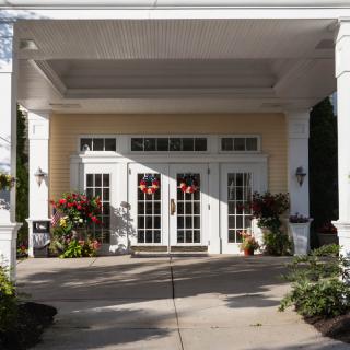 A welcoming entrance with white pillars and large glass doors, adorned with plants and flowers.