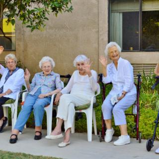A group of elderly women sitting outdoors, waving and enjoying the day.