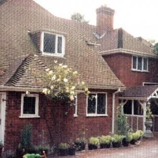 A charming brick house with a sloping roof and several windows, adorned with plants in the front.