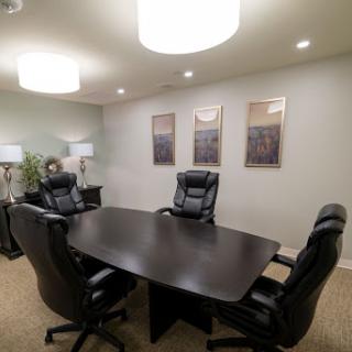 A modern conference room featuring a dark wooden table surrounded by black leather chairs, illuminated by stylish overhead lights.