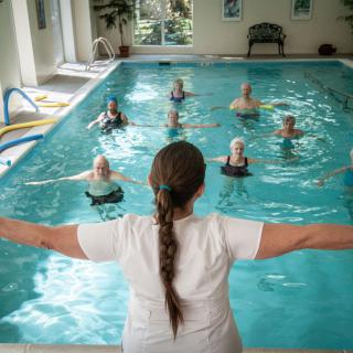 An instructor leads a group of seniors in a water aerobics class at an indoor pool.